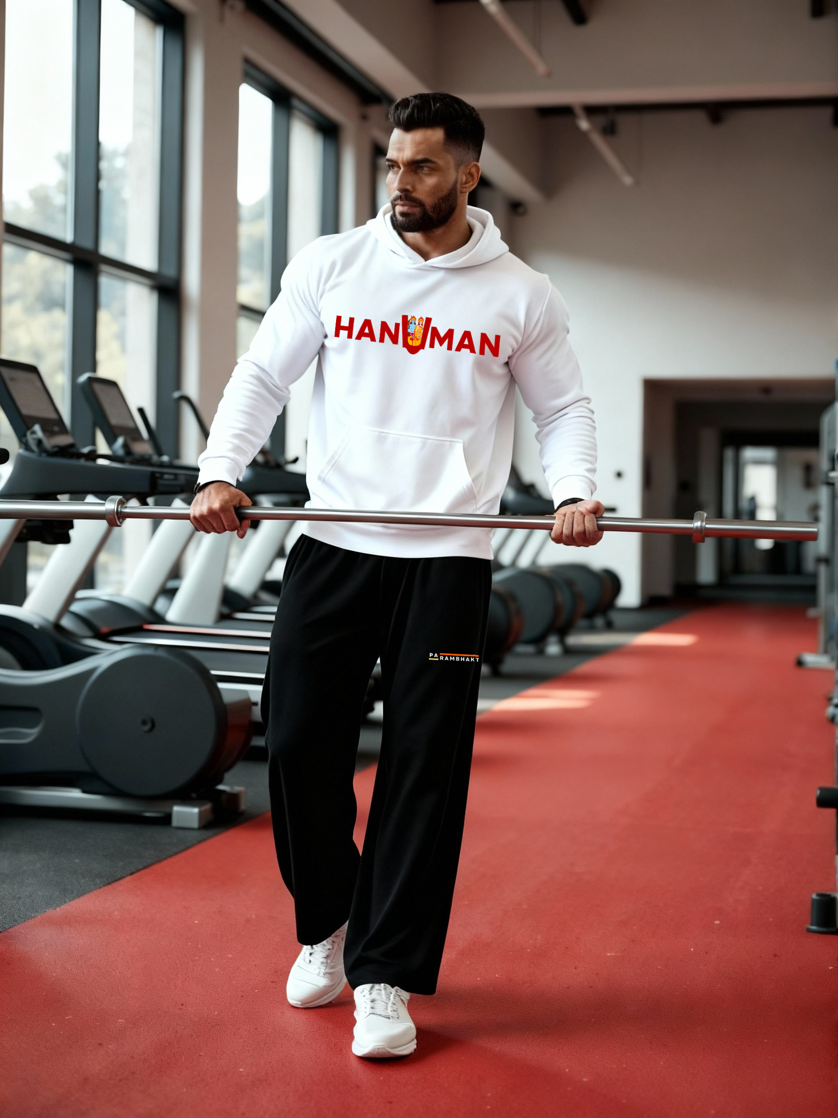 Man wearing a white Parambhakt ‘Hanuman in U’ Training Hoodie holding a barbell while walking inside a gym.