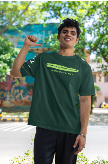 Man wearing a green hanuman's way oversized t-shirt by Parambhakt, standing outdoors with trees and buildings in the background.