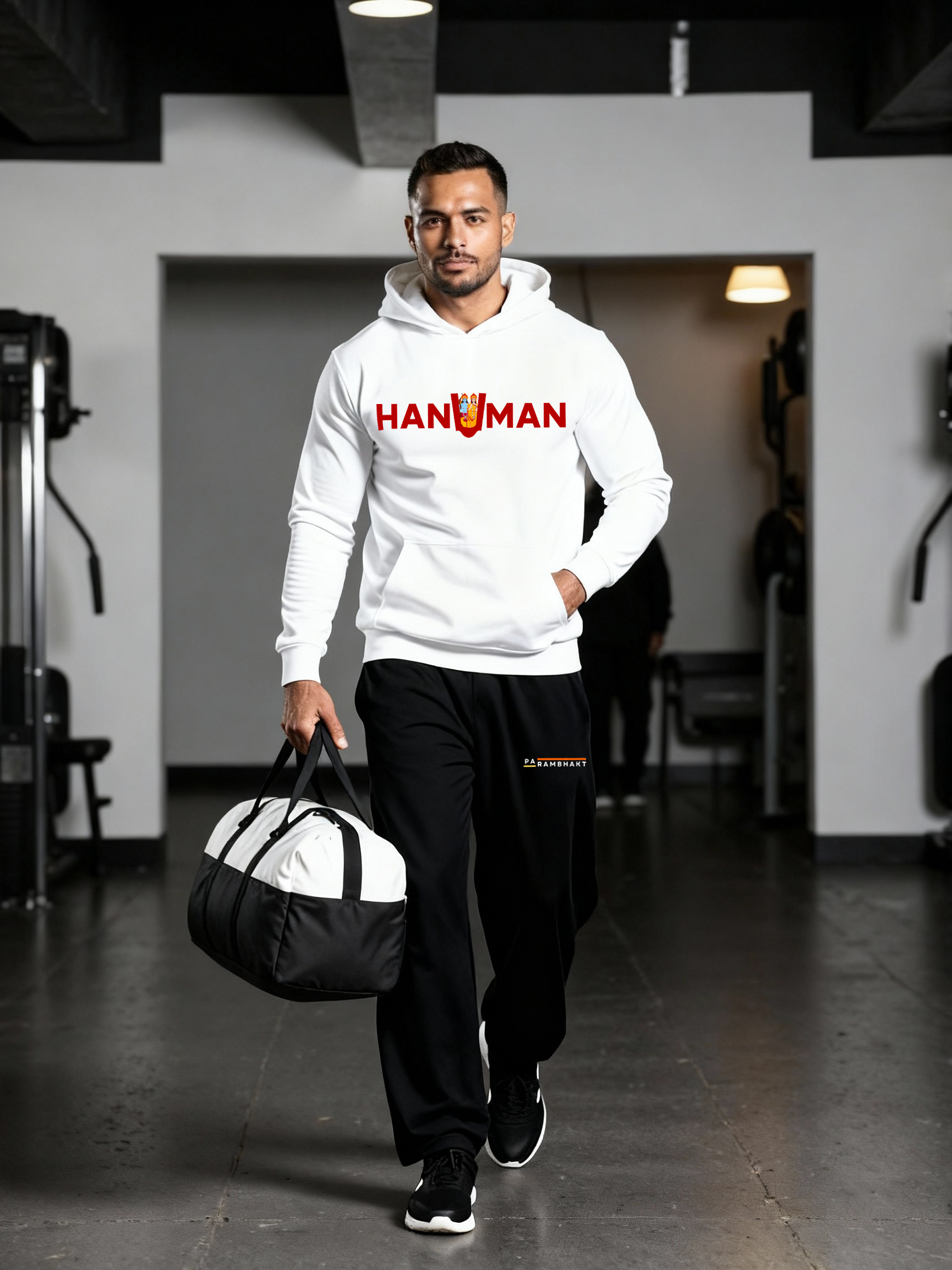 Man wearing a white Parambhakt ‘Hanuman in U’ Training Hoodie walking inside a gym with a duffel bag.