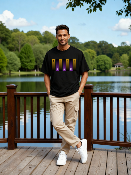 Man at a wooden lakeside deck wearing Parambhakt Shri Ram oversized T-shirt in a casual outdoor look.
