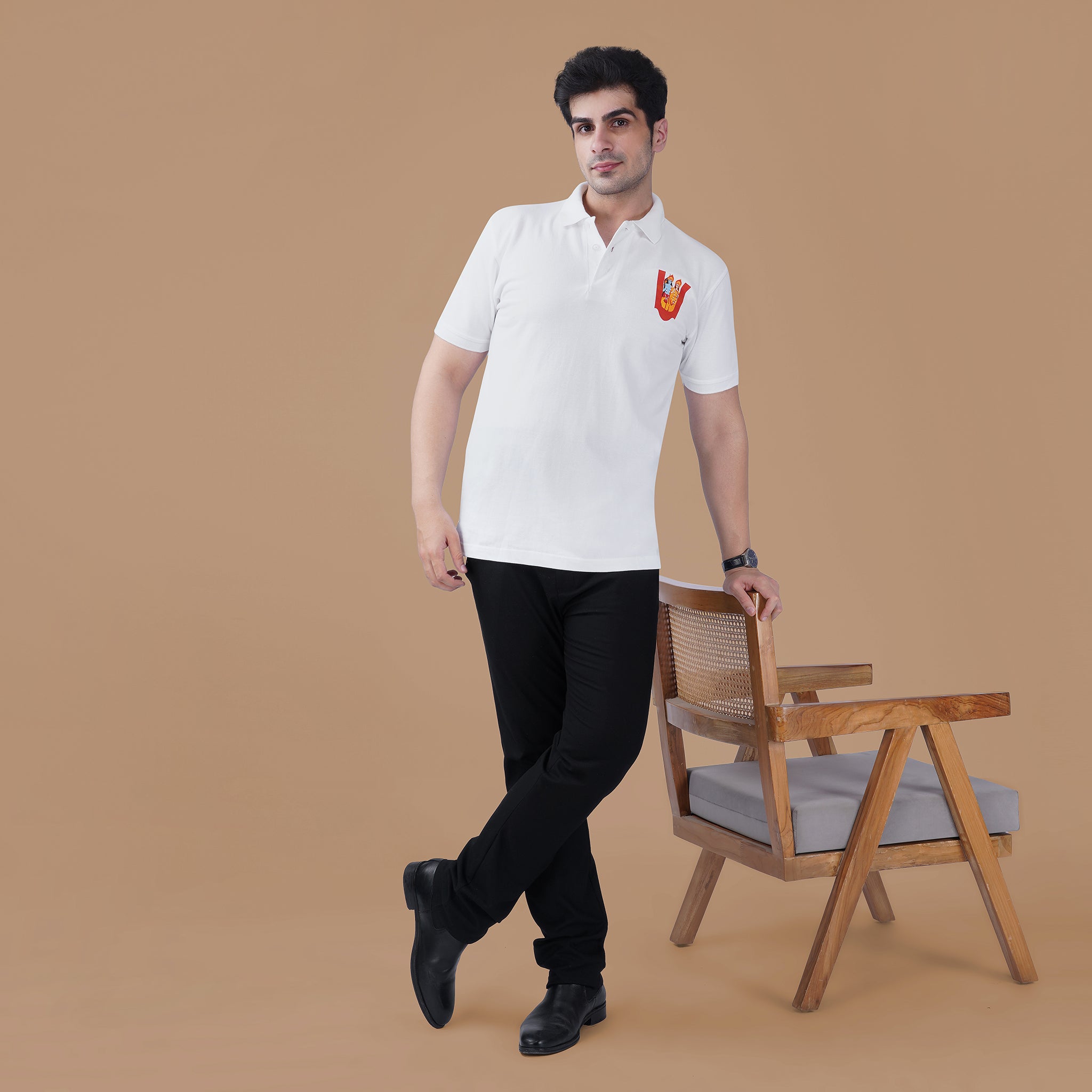 Man wearing the white Parambhakt Siya Ram Tilak Polo standing beside a wooden chair, showcasing a modern spiritual lifestyle look.