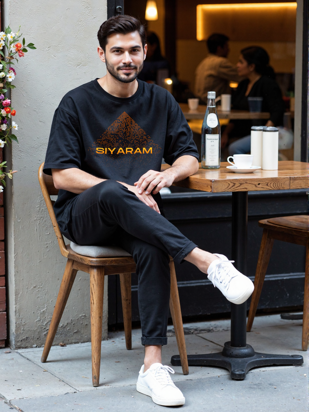 Man at a café wearing Parambhakt Siyaram oversized T-shirt, styled in a modern casual look.